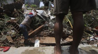 Warga membersihkan puing-puing reruntuhan di rumahnya yang tertimpa tanah longsor di Kelurahan Bangka, Mampang Prapatan, Jakarta, Minggu (21/2/2021). [Suara.com/Angga Budhiyanto]