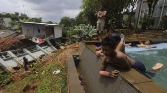 Sejumlah anak berenang di dekat lokasi tanah longsor yang menimpa rumah warga di Kelurahan Bangka, Mampang Prapatan, Jakarta, Minggu (21/2/2021). [Suara.com/Angga Budhiyanto]