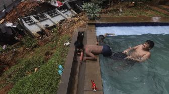 Sejumlah anak berenang di dekat lokasi tanah longsor yang menimpa rumah warga di Kelurahan Bangka, Mampang Prapatan, Jakarta, Minggu (21/2/2021). [Suara.com/Angga Budhiyanto]