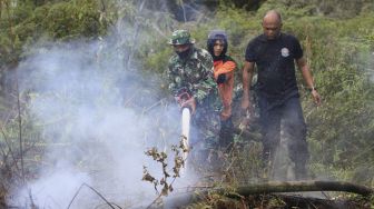 Personel TNI Ad bersama petugas pemadam kebakaran memadamkan api yang membakar lahan gambut di kawasan perbatasan Kabupaten Aceh Barat dan Kabupaten Nagan Raya, Aceh, Minggu (28/2/2021). [ANTARA FOTO/Syifa Yulinnas]