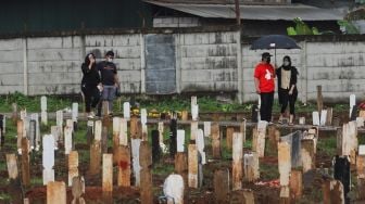 Warga berziarah ke makam kerabatnya di area khusus pemakaman Covid-19 yang terisi penuh di TPU Bambu Apus , Jakarta Timur, Sabtu (6/3/2021). [Suara.com/Alfian Winanto]