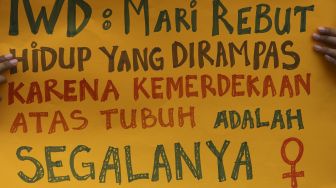 Seorang massa yang tergabung dalam Perempuan Mahardhika membawa poster saat melakukan aksi memperingati Hari Perempuan Internasional di kawasan Patung Kuda Arjuna Wiwaha, Jakarta, Senin (8/3/2021). [Suara.com/Angga Budhiyanto]