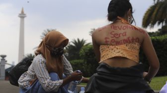 Seorang massa yang tergabung dalam Perempuan Mahardhika membeli air mineral si sela-sela melakukan aksi memperingati Hari Perempuan Internasional di kawasan Patung Kuda Arjuna Wiwaha, Jakarta, Senin (8/3/2021). [Suara.com/Angga Budhiyanto]
