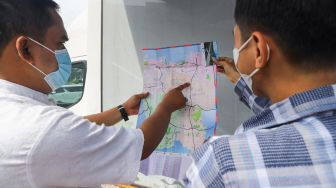 Petugas Dinas Pariwisata dan Ekonomi Kreatif DKI Jakarta menjelaskan tentang destinasi wisata dengan menggunakan peta kepada warga saat uji coba Tourist Information Center Mobile (TICM) di Terminal Blok M, Jakarta Selatan, Jumat (12/3/2021). [Suara.com/Alfian Winanto]
