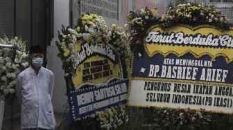 Salah seorang kerabat berdiri di dekat karangan bunga tanda berduka cita atas meninggalnya Mantan Jaksa Agung Basrief Arief di rumah duka di kawasan Petogogan, Kebayoran Baru, Jakarta, Selasa (23/3/2021). [Suara.com/Angga Budhiyanto]