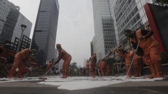 Petugas gabungan Unit Kerja Perangkat Daerah (UKPD) membersihkan trotoar sepanjang Jalan Sudirman-Thamrin, Jakarta, Sabtu (27/3/2021). [Suara.com/Angga Budhiyanto]