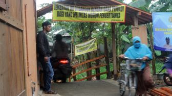 Seorang Ibu mendorong sepedahnya saat melintasi jembatan alternatif, Tambun Selatan, Kabupaten Bekasi (30/03/21). [Suara.com/Dian Latifah]
