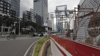 Pesepeda melintas di dekat proyek pembangunan Tugu Sepeda di Jalan Jenderal Sudirman, Jakarta, Senin (5/4/2021). [Suara.com/Angga Budhiyanto]