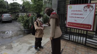 Seorang Guru mengukur suhu tubuh murid pada hari pertama uji coba pembelajaran tatap muka di SD Negeri Kenari 08 Pagi, Jakarta, Rabu (7/4/2021). [Suara.com/Angga Budhiyanto]