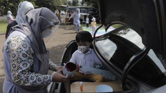 Seorang siswa taman kanak-kanak (TK) didampingi orang tuanya membuat miniatur beduk saat mengikuti proses pembelajaran secara Drive in Learning (DRIL) di area parkir Padepokan Pencak Silat Indonesia, Jakarta, Kamis (8/4/2021). [Suara.com/Angga Budhiyanto]