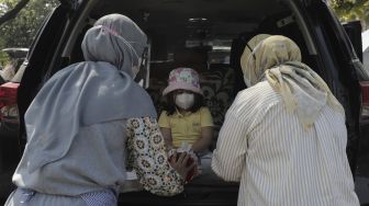 Seorang siswa taman kanak-kanak (TK) didampingi orang tua dan guru membuat miniatur beduk saat mengikuti proses pembelajaran secara Drive in Learning (DRIL) di area parkir Padepokan Pencak Silat Indonesia, Jakarta, Kamis (8/4/2021). [Suara.com/Angga Budhiyanto]