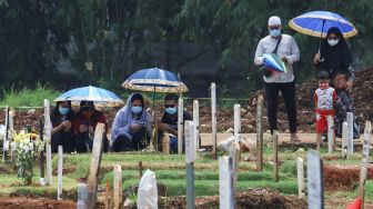 Warga berdoa diatas pusara kerabatnya saat ziarah di  area pemakaman khusus Covid - 19 TPU Bambu Apus, Jakarta Timur, Minggu (11/4/2021). [Suara.com/Alfian Winanto]