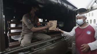 Petugas membagikan takjil kepada personel Satpol PP dengan sistem drive thru di kompleks Masjid Al-Azhar, Jakarta, Rabu (14/4/2021). [Suara.com/Angga Budhiyanto]