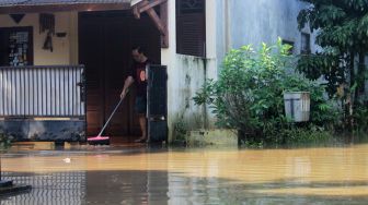 Warga membersihkan rumahnya saat air mulai surut di Perumahan Bumi Nasio Indah, Bekasi, Kamis (15/4/2021).[Suara.com/Dian Latifah]