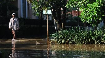 Warga melintas di genangan banjir Perumahan Bumi Nasio Indah, Bekasi, Kamis (15/4/2021). [Suara.com/Dian Latifah]