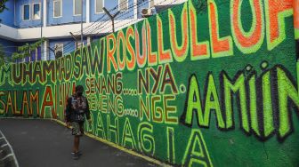 Warga berjalan di depan mural bernuansa Islami di Gang Pelangi, Kalibata, Jakarta Selatan, Sabtu (17/4/2021). [Suara.com/Alfian Winanto]