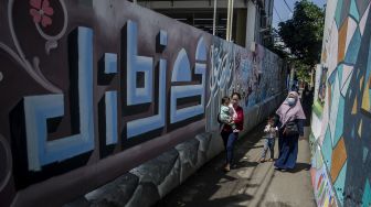 Warga melintas di depan mural kaligrafi di Kampung Wisata Budaya Kaligrafi di Bandung, Jawa Barat, Jumat (16/4/2021).  ANTARA FOTO/Novrian Arbi