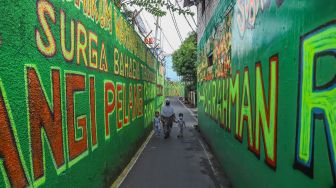 Warga berjalan diantara dinding dengan mural bernuansa Islami di Gang Pelangi, Kalibata, Jakarta Selatan, Sabtu (17/4/2021). [Suara.com/Alfian Winanto]