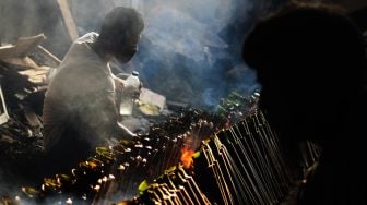 Pekerja merapihkan nasi lemang yang sedang dibakar, di kawasan Senen, Jakarta Pusat, Senin (19/4/2021). [Suara.com/Dian Latifah]
