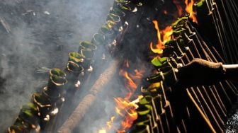 Pembuat merapihkan nasi lemang yang sedang dibakar, di kawasan Senen, Jakarta Pusat, Senin (19/4/2021). [Suara.com/Dian Latifah]