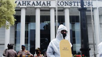 Pendemo membawa replika batu nisan sebagai bagian dari teatrikal yang dilakukan di  Mahkamah Konstitusi, Jakarta Pusat, Rabu (21/4/2021).  [Suara.com/Dian Latifah]   