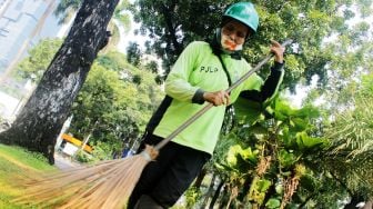 Ibu Asiah menyapu di tengah taman di Jalan Medan Merdeka Selatan, Jakarta Pusat, Kamis (22/4/2021). [Suara.com/Dian Latifah]