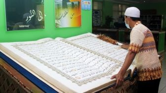 Petugas membersihkan Al-quran besar di Perpustakaan Jakarta Islamic Centre (JIC), Jakarta Utara, Kamis (22/4/2021).  [Suara.com/Dian Latifah]

