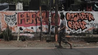 Seorang warga berjalan melintasi mural Persija Jakarta di kawasan Pasar Minggu, Jakarta, Senin (26/4/2021). [Suara.com/Angga Budhiyanto]