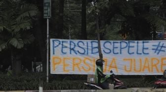 Pengendara sepeda motor berhenti di depan spanduk Persija Jakarta juara Piala Menpora 2021 yang terpasang di kawasan Pasar Minggu, Jakarta, Senin (26/4/2021). [Suara.com/Angga Budhiyanto]