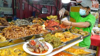 Pedagang nasi kapau melayani pembeli di Food Street Kramat di Kawasan Senen, Jakarta Pusat, Selasa (27/4/2021). [Suara.com/Alfian Winanto]