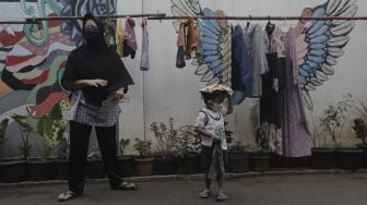 Seorang anak menerima pakaian bekas layak pakai yang dijajakan secara gratis di Jalan Jati Padang VI RT 002 RW 004, Pasar Minggu, Jakarta Selatan, Rabu (28/4/2021). [Suara.com/Angga Budhiyanto]