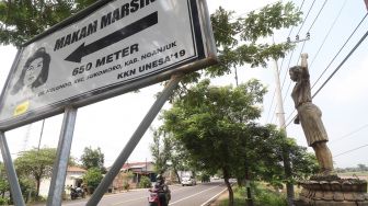 Pengendara sepeda motor melintas di depan patung pejuang buruh Marsinah sebagai petunjuk arah makam di Desa Nglundo, Nganjuk, Jawa Timur, Sabtu (1/5/2021). ANTARA FOTO/Prasetia Fauzani