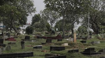 Petugas membersihkan makam di Tempat Pemakaman Umum (TPU) Karet Bivak, Jakarta, Rabu (12/5/2021). [Suara.com/Angga Budhiyanto]