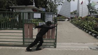 Petugas keamanan menutup pintu masuk ke Tempat Pemakaman Umum (TPU) Karet Bivak, Jakarta, Rabu (12/5/2021). [Suara.com/Angga Budhiyanto]