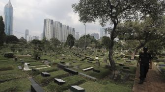 Petugas keamanan berjaga di area makam di Tempat Pemakaman Umum (TPU) Karet Bivak, Jakarta, Rabu (12/5/2021). [Suara.com/Angga Budhiyanto]