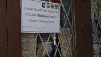 Seorang warga yang baru kembali ke Jakarta berdiri di balik stiker tanda menjalani isolasi mandiri di rumahnya di kawasan Lenteng Agung, Jakarta, Senin (17/5/2021). [Suara.com/Angga Budhiyanto]