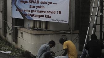 Pekerja memperbaiki instalasi kabel di dekat spanduk peringatan untuk pemudik di kawasan Tegal Parang, Jakarta, Senin (17/5/2021). [Suara.com/Angga Budhiyanto]