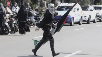 Seorang massa aksi berjalan membawa bendera Palestina saat mengikuti aksi solidaritas dukung Palestina terkait kekerasan yang terjadi beberapa waktu lalu oleh Israel di depan Kedubes AS, Jakarta, Selasa (18/5/2021). [Suara.com/Angga Budhiyanto]