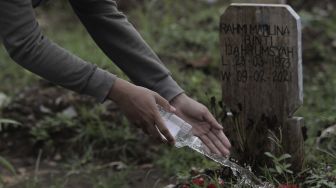 Warga menyiramkan air ke makam keluarganya saat melakukan ziarah kubur di pemakaman khusus COVID-19 di TPU Srengseng Sawah, Jakarta, Selasa (18/5/2021). [Suara.com/Angga Budhiyanto]