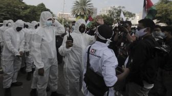 Polisi memakai baju hazmat memberi imbauan kepada massa yang mengikuti aksi solidaritas dukung Palestina di depan Kedubes AS, Jakarta, Selasa (18/5/2021). [Suara.com/Angga Budhiyanto]