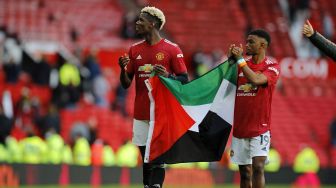 Pemain Manchester United Paul Pogba dan Amad Diallo mengibarkan bendera Palestina usai laga kontra Fulham yang berakhir imbang dalam lanjutan Liga Inggris di Old Trafford, Manchester, Inggris, Selasa (18/5/2021).  Laurence Griffiths / POOL / AFP
