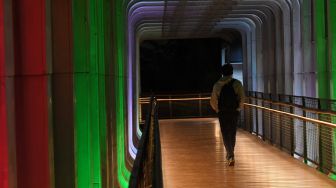 Warga melintasi jembatan penyebrangan orang (JPO) Polda Metro Jaya yang berhias lampu berwarna bendera Palestina di Jakarta, Rabu (19/5/2021). ANTARA FOTO/Akbar Nugroho Gumay
