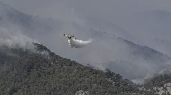 Sebuah pesawat pemadam kebakaran menjatuhkan air untuk memadamkan api liar di dekat desa Alepochori, selatan Athena, pada pada (20/5/2021). [Louisa GOULIAMAKI / AFP]