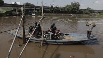 Sejumlah pengendara sepeda motor menggunakan perahu eretan untuk menyeberangi Kali Cagak, Jakarta Utara, Selasa (25/5/2021). [Suara.com/Angga Budhiyanto]