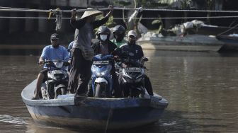 Sejumlah pengendara sepeda motor menggunakan perahu eretan untuk menyeberangi Kali Cagak, Jakarta Utara, Selasa (25/5/2021). [Suara.com/Angga Budhiyanto]