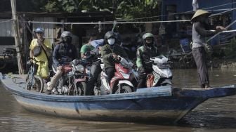 Sejumlah pengendara sepeda motor menggunakan perahu eretan untuk menyeberangi Kali Cagak, Jakarta Utara, Selasa (25/5/2021). [Suara.com/Angga Budhiyanto]