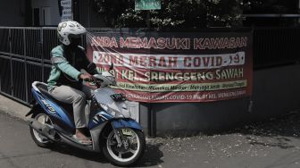 Pengendara sepeda motor melintasi spanduk penanda zona merah di Jalan H Shibi II, Kelurahan Srengseng Sawah, Jagakarsa, Jakarta Selatan, Jumat (28/5/2021). [Suara.com/Angga Budhiyanto]