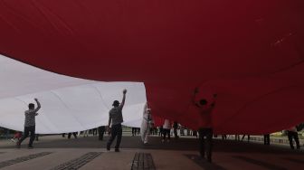 Massa menyemprtokan cairan disinfektan saat pengibaran bendera merah putih raksasa di kawasan Patung Kuda Arjuna Wiwaha, Jakarta, Rabu (2/6/2021). [Suara.com/Angga Budhiyanto]