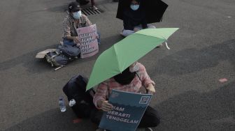 Aktivis lingkungan hidup membawa poster saat melakukan aksi Jeda Untuk Iklim di kawasan Patung Kuda Arjuna Wiwaha, Jakarta, Jumat (4/6/2021). [Suara.com/Angga Budhiyanto]