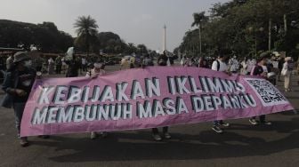 Sejumlah aktivis lingkungan hidup membentangkan spanduk saat melakukan aksi Jeda Untuk Iklim di kawasan Patung Kuda Arjuna Wiwaha, Jakarta, Jumat (4/6/2021). [Suara.com/Angga Budhiyanto]